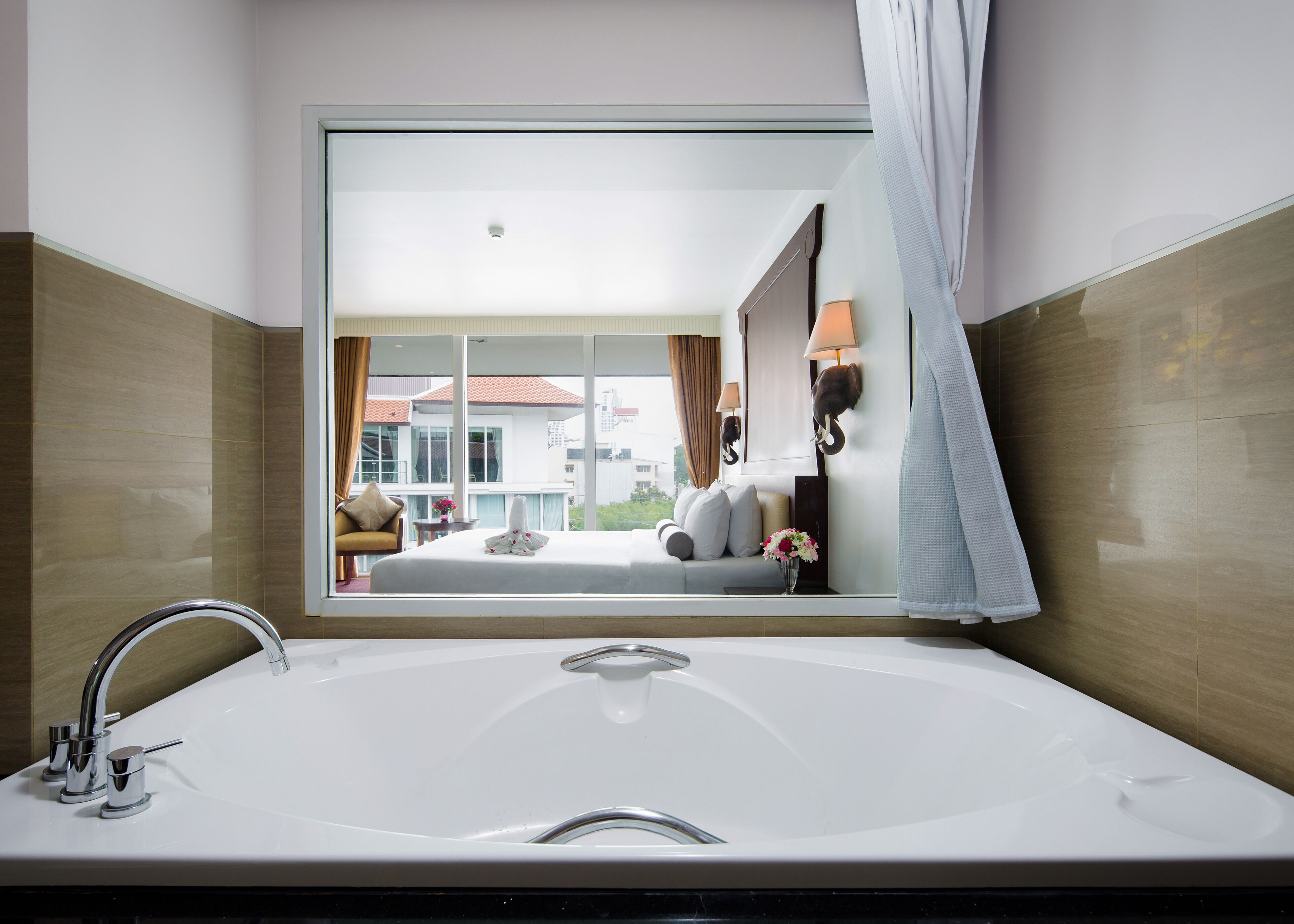 A modern bathroom with a large bathtub, a vanity with a mirror, and a view of a balcony with a sofa and cushions.