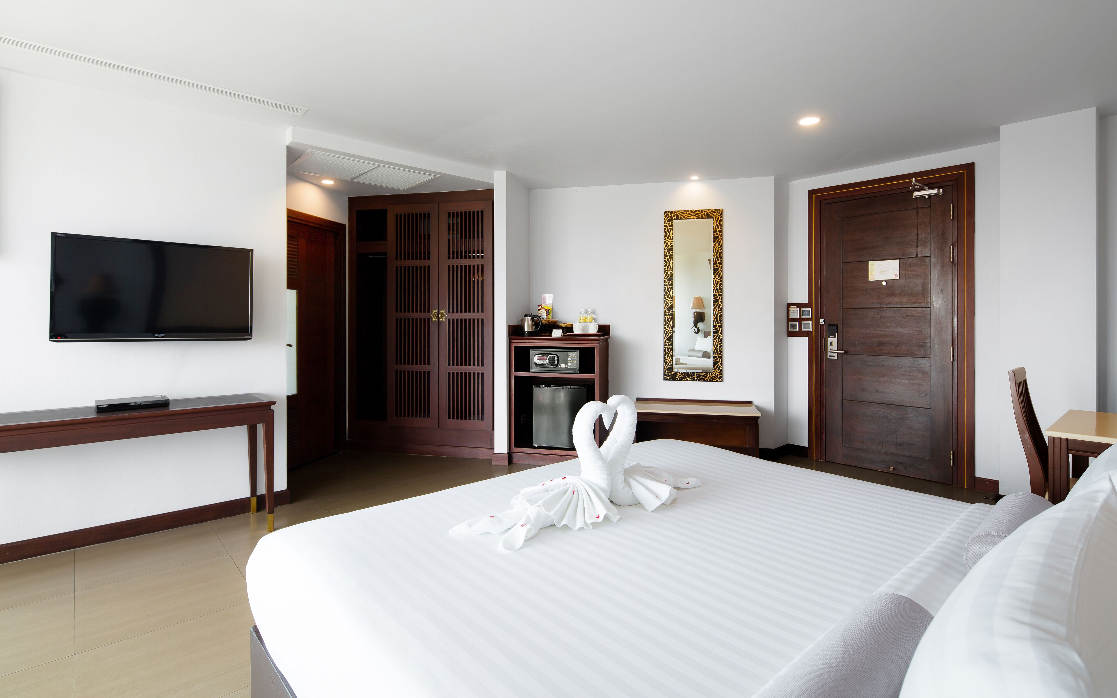 A hotel room with a bed, a television, a desk, a wardrobe, and a door.
