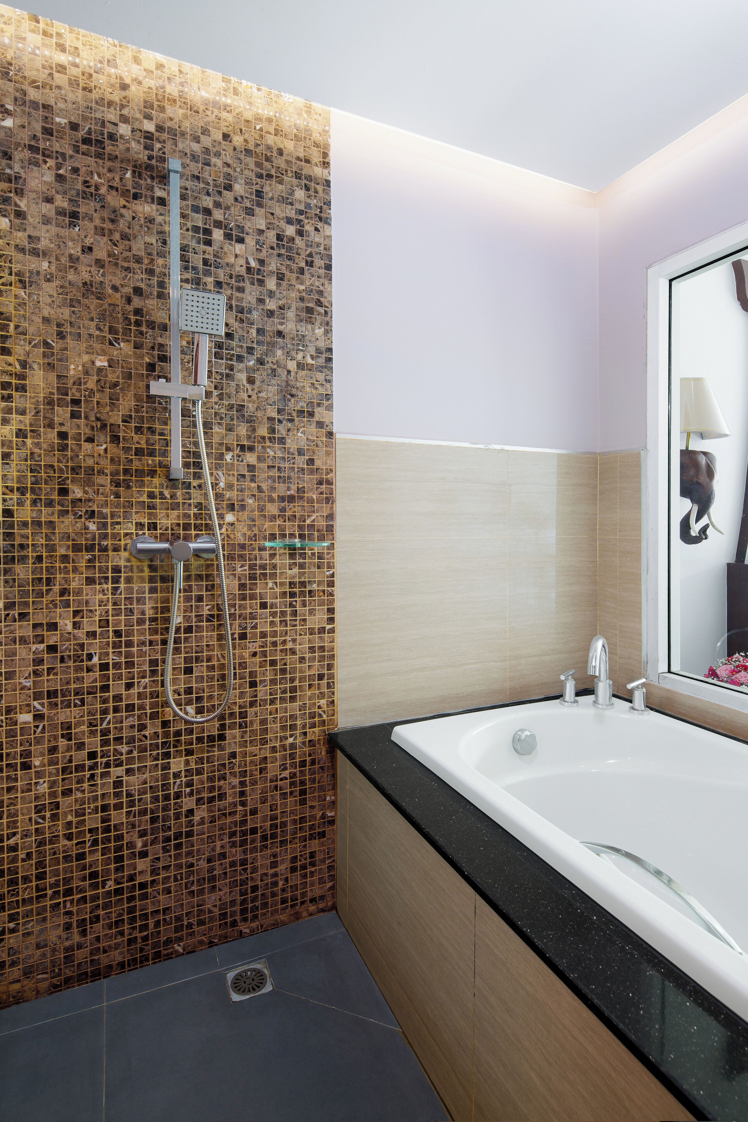 Une salle de bain moderne avec un mur recouvert de mosaïques, une baignoire sur pieds et un miroir avec une lampe.