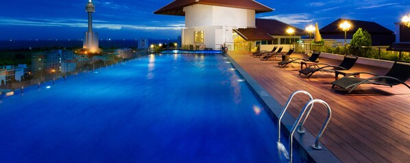A swimming pool with lounge chairs and a view of a tower and buildings at dusk. - Aiyara Grand Hotel (Pattaya)