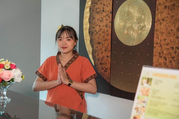 A person standing in front of a reception desk with a decorative wall behind them. - Aiyara Grand Hotel (Pattaya)