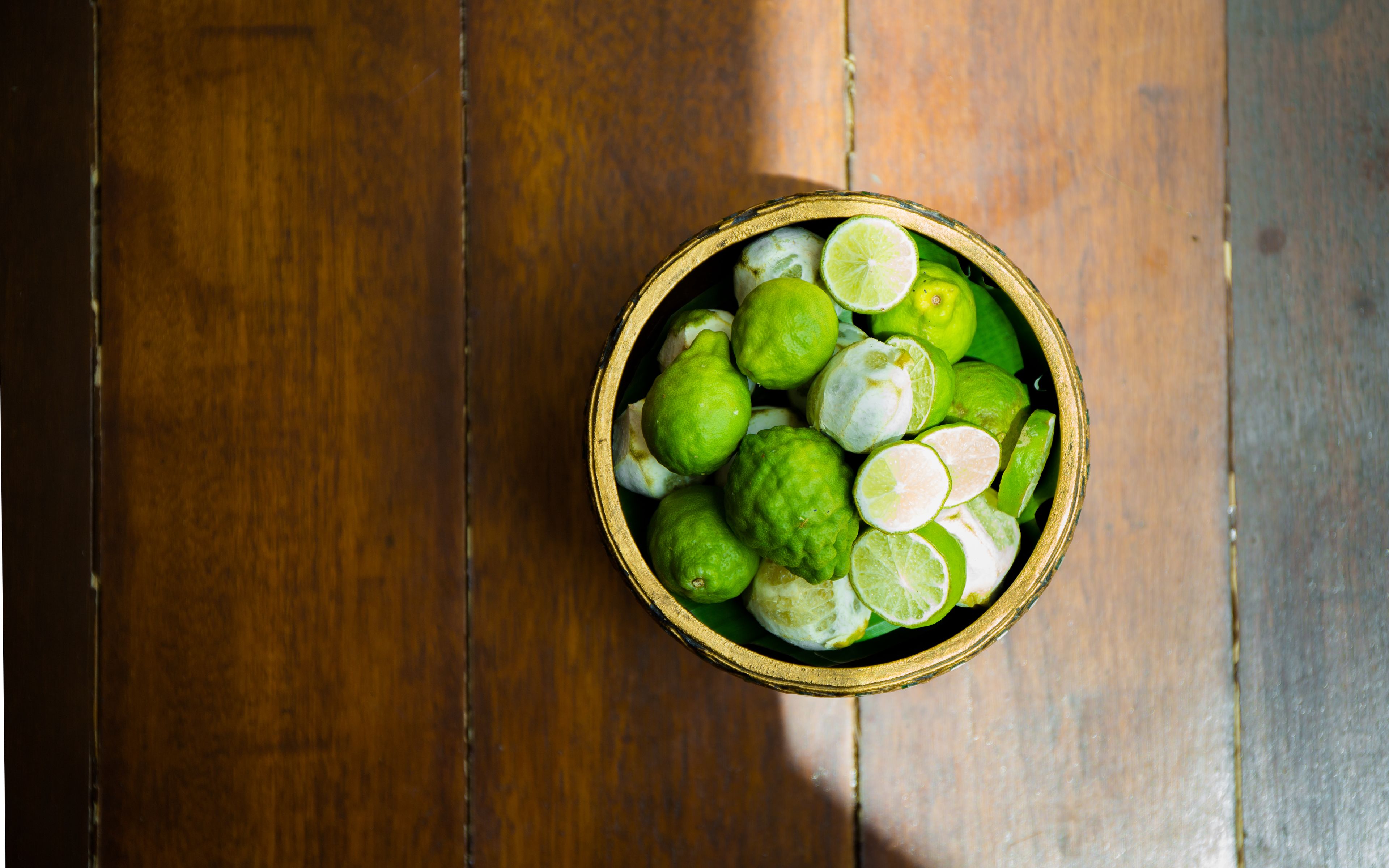 A wooden table with a bowl containing limes and lime slices.
