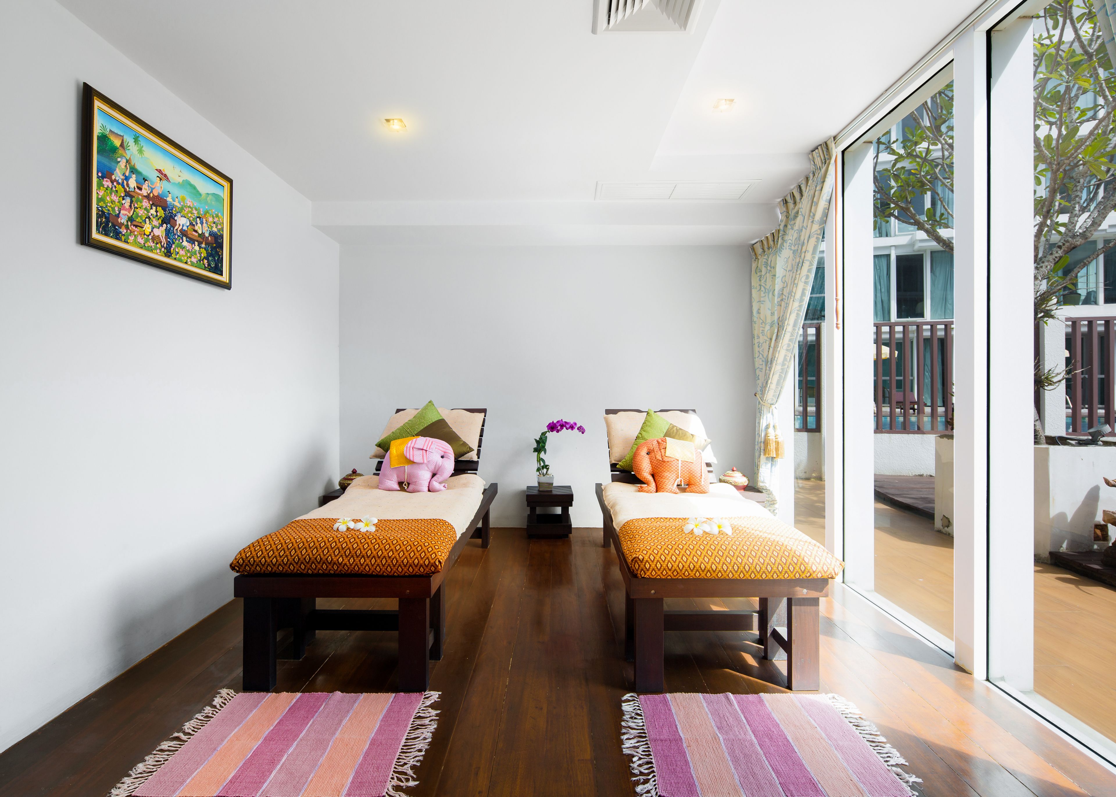 A room with two beds, a painting on the wall, and a view of the outside.