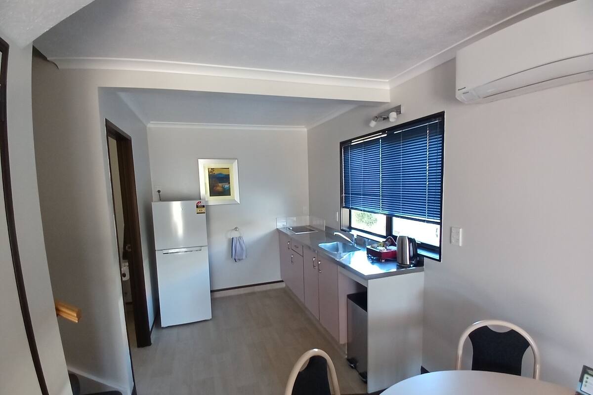 A compact kitchen with a refrigerator, sink, and window with blinds.