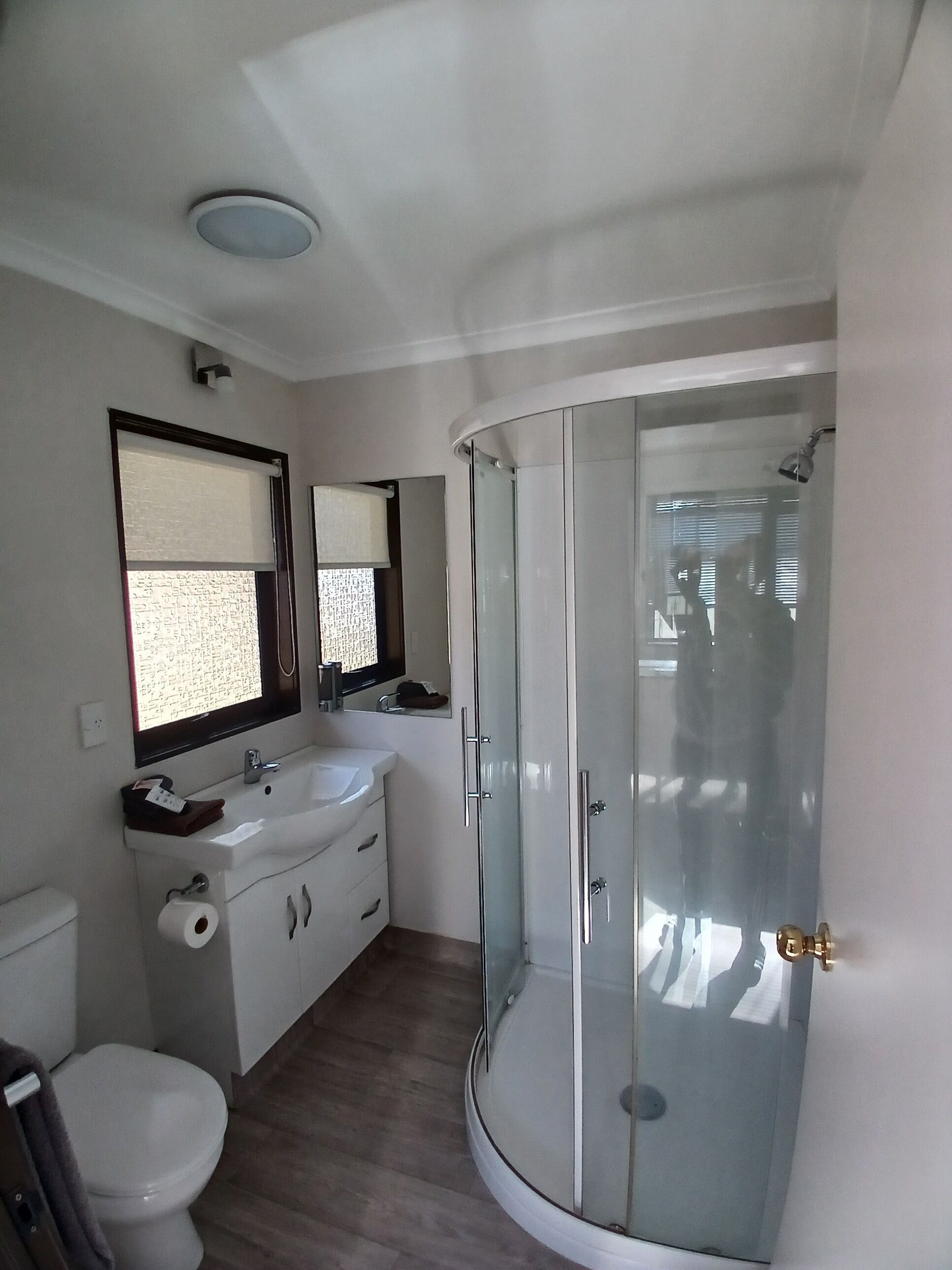 Een moderne badkamer met een glazen douchecabine, een witte wastafel en een toilet.