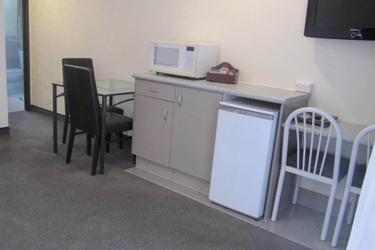 A compact kitchenette with a microwave, a small refrigerator, a sink, and a chair.