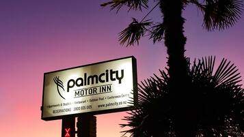 Señal del motel Palmcity Inn, con un letrero de neón que dice 'VACANCY' debajo, frente a un cielo de atardecer con palmeras.