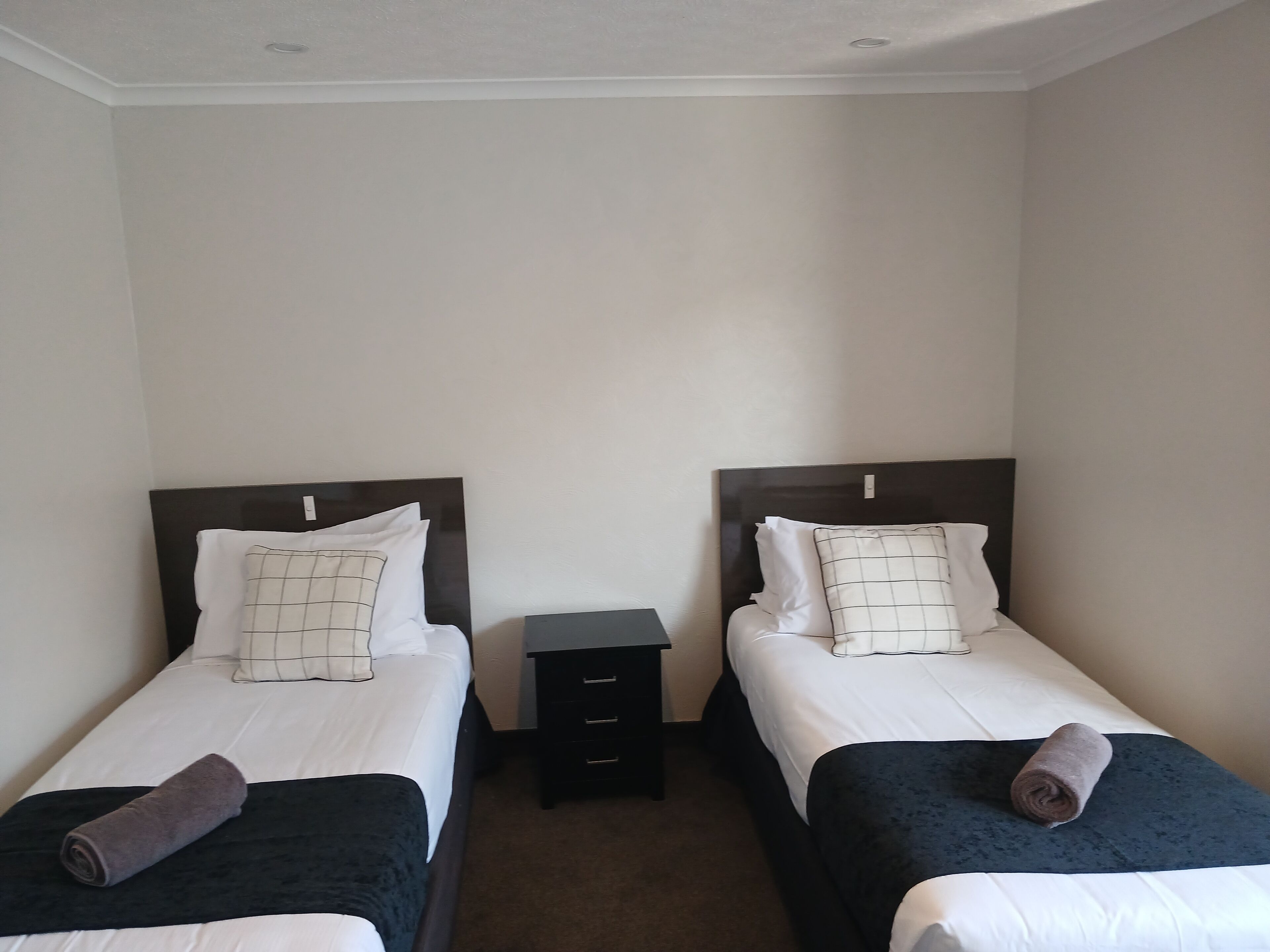 Habitación doble con dos camas individuales, cada una con una almohada y una toalla enrollada.