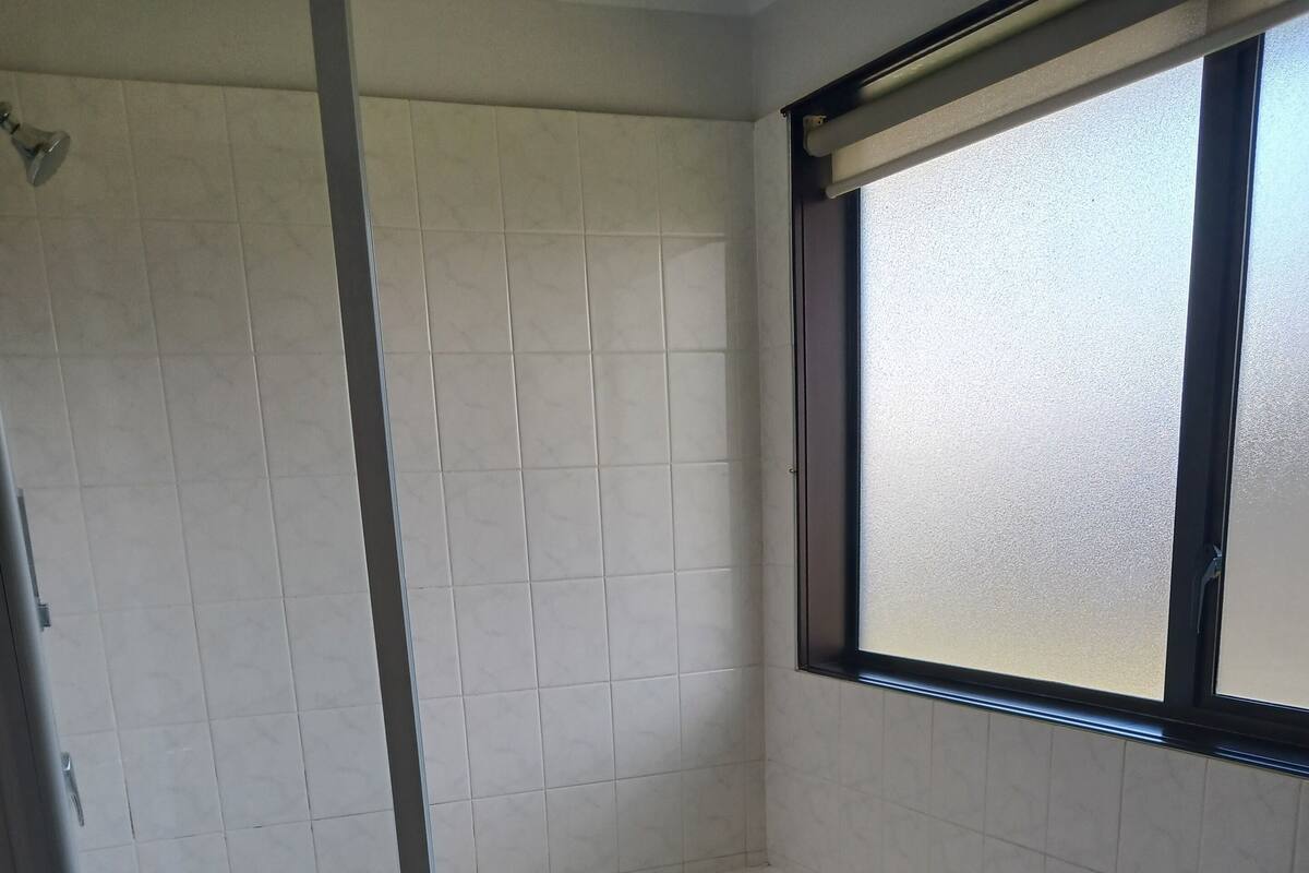 A corner bathroom with a freestanding bathtub, a window, and a vent.