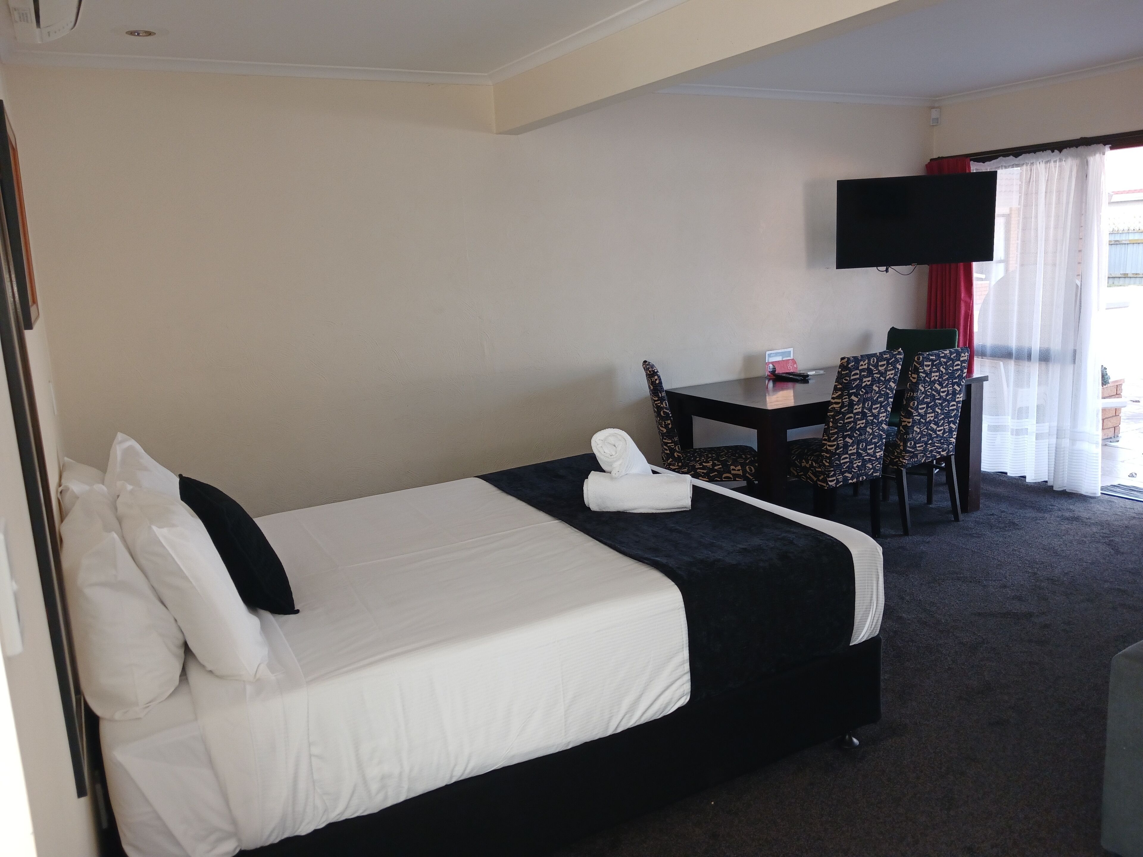A hotel room with a bed, a desk, a chair, a TV, and a window with curtains.
