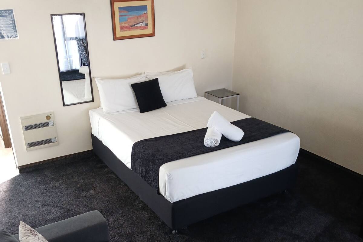 A hotel room with a bed, a bedside table, a small table, a sofa, a mirror, and a picture on the wall.