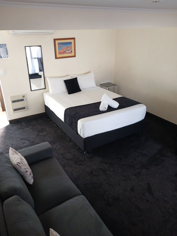 A hotel room with a bed, a bedside table, a small table, a sofa, a mirror, and a picture on the wall. - Palm City Motor Inn (Napier)