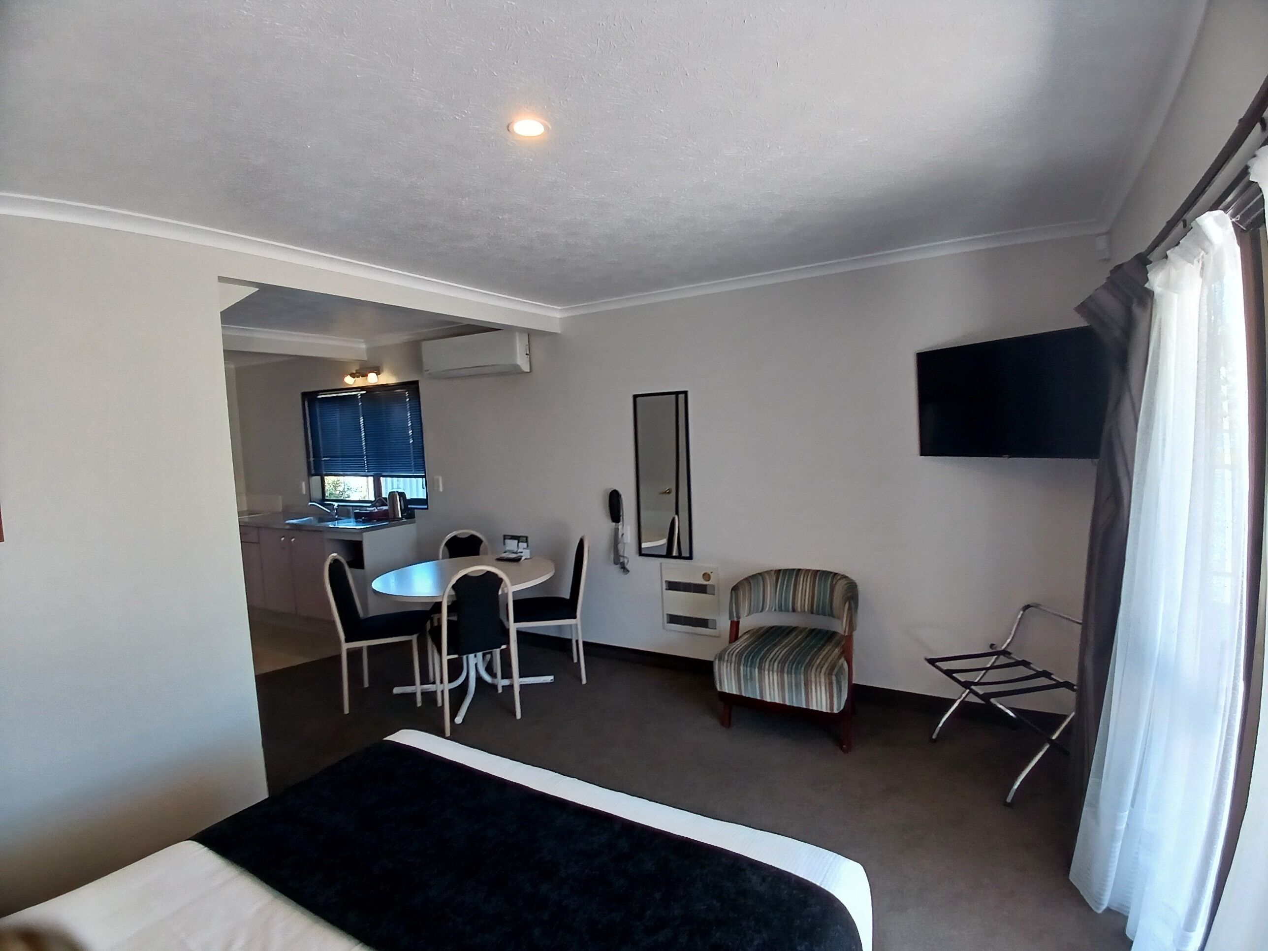 A hotel room with a bed, a desk with chairs, a television, and a window with curtains.