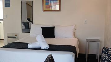 A hotel room with a bed, a bedside table, a mirror, a framed picture on the wall, and a fire action notice.