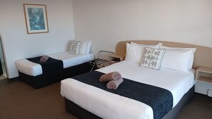 Ein Hotelzimmer mit zwei Einzelbetten, jeweils mit Kissen und zusammengelegtem Handtuch. Ein kleiner Nachttisch mit Lampe, eine Wandsteckdose und ein gerahmtes Bild sind ebenfalls vorhanden.