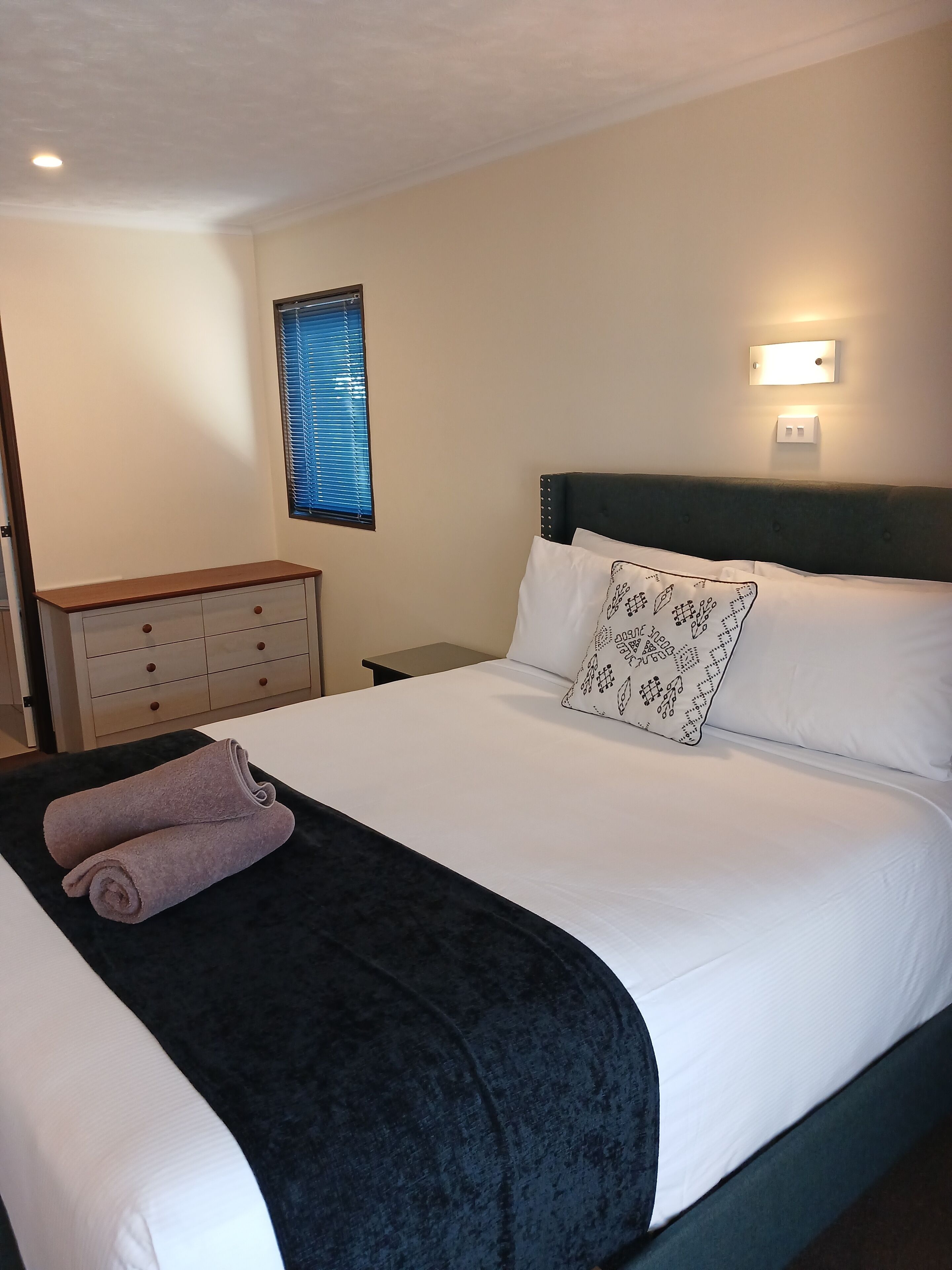 A neatly made bed with a dark headboard, white bedding, and a patterned pillow.