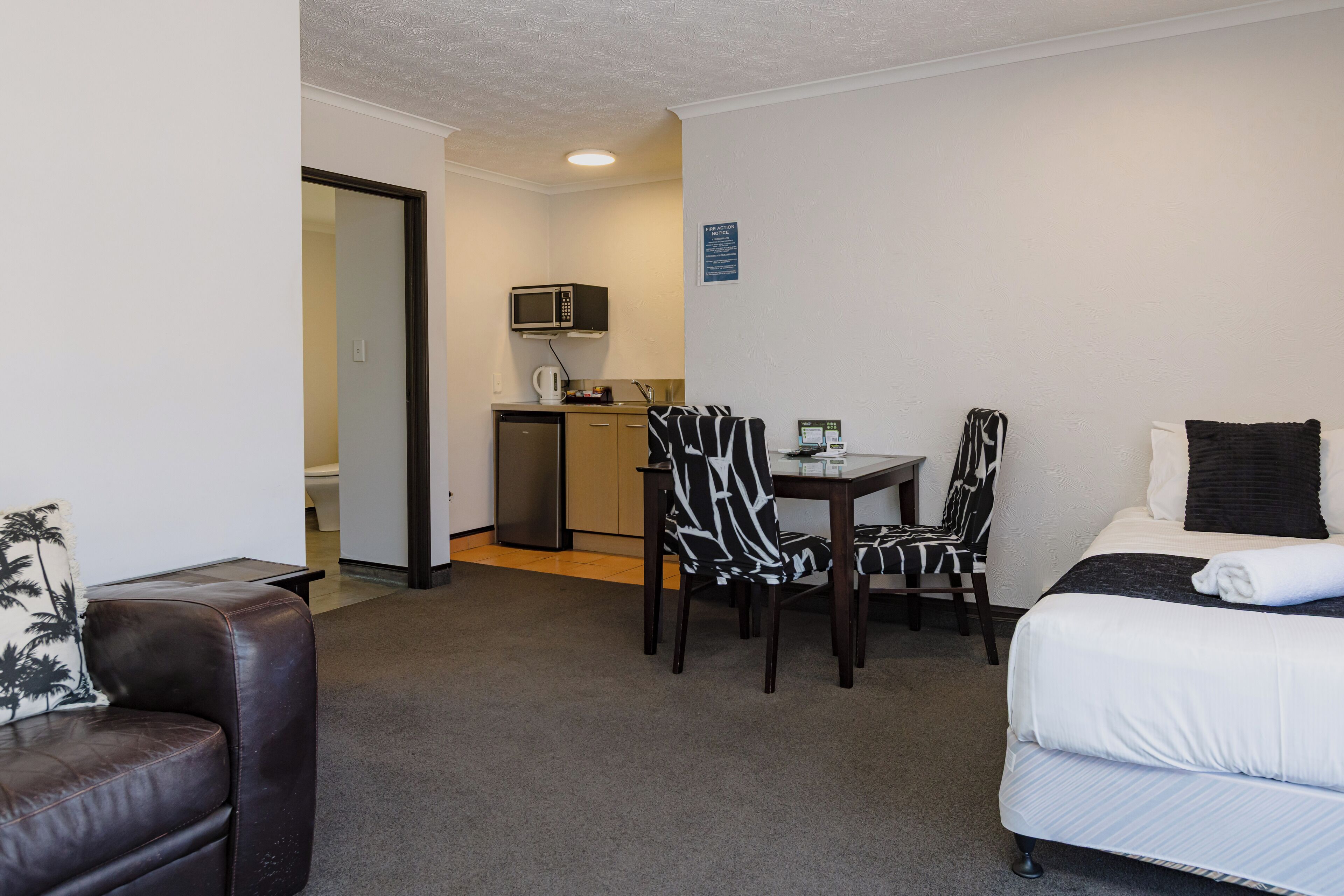 Una habitación de hotel con cama, una mesa de comedor con sillas, microondas y una pequeña kitchenette.