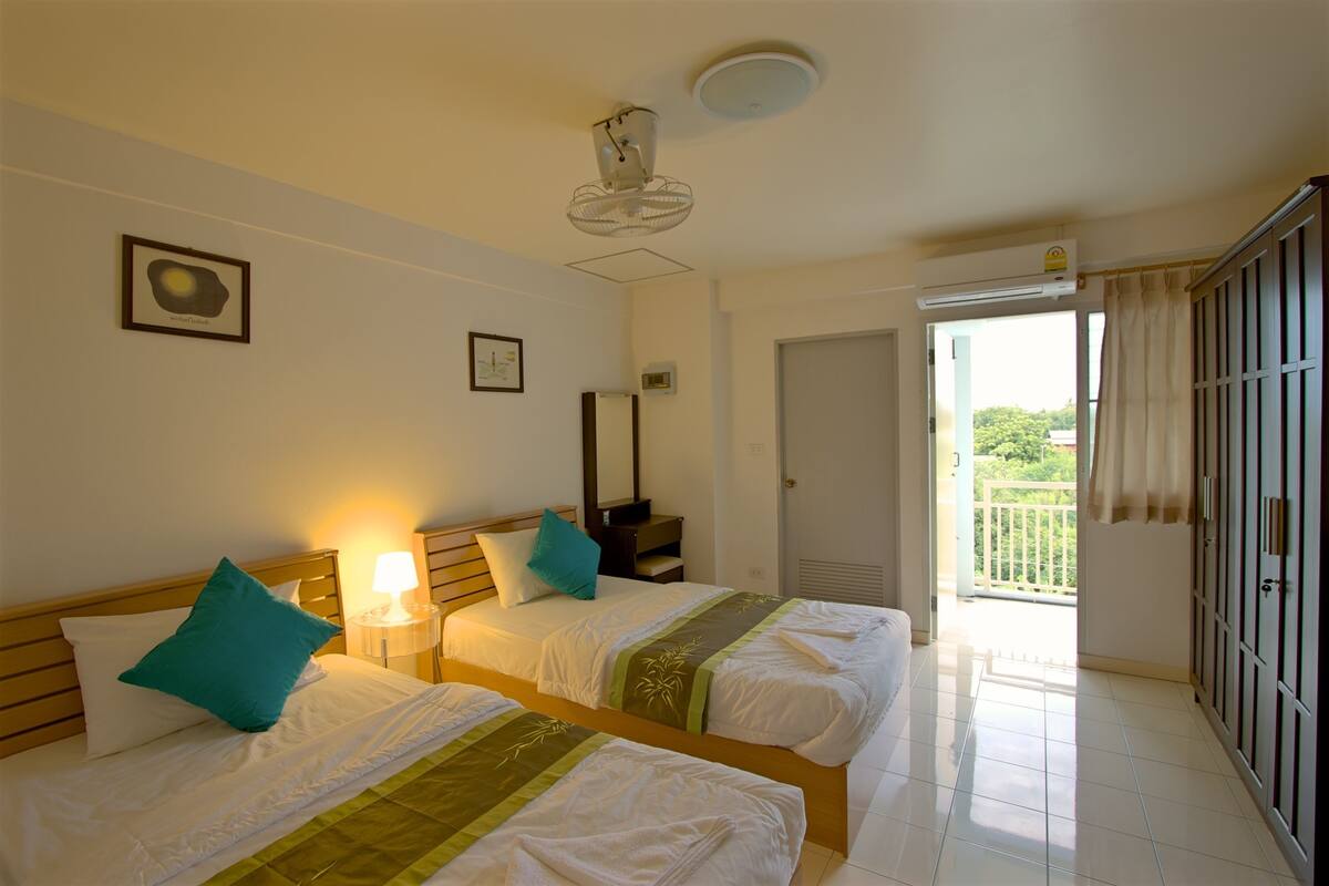 A hotel room with two beds, a ceiling fan, a nightstand, a lamp, and a door leading to a balcony.