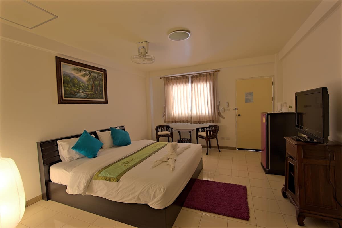 A hotel room with a bed, a desk, a chair, a television, and a painting on the wall.