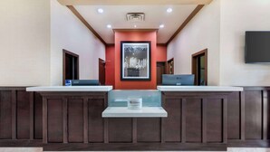 A reception area with two reception desks, a framed cityscape picture on the wall, and a flat-screen TV above the desks. - Best Western Pacific Inn (Vernon)