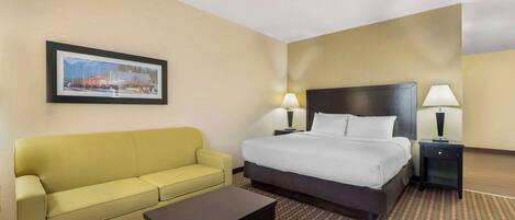 A hotel room with a bed, a yellow sofa, a small table, two bedside lamps, and a framed picture on the wall.