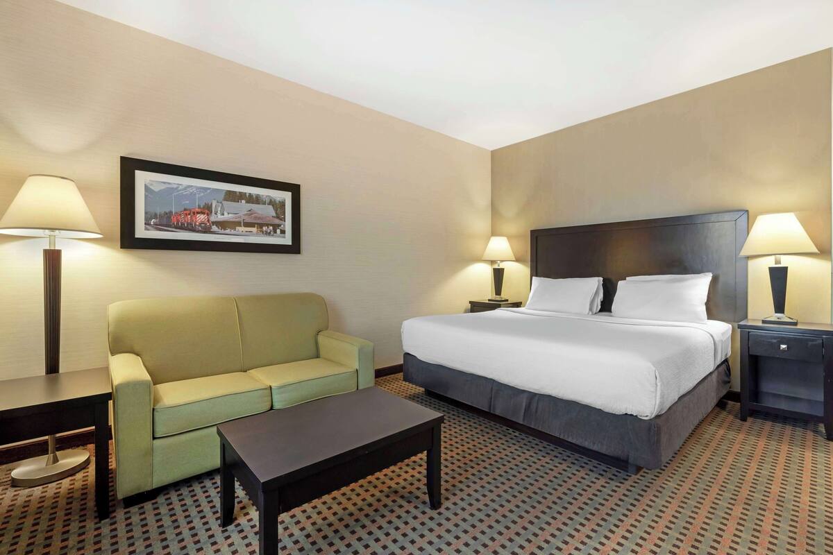 A hotel room with a bed, a sofa, a coffee table, two bedside tables with lamps, and a framed picture on the wall.