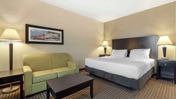 A hotel room with a bed, a sofa, a coffee table, two bedside tables with lamps, and a framed picture on the wall.