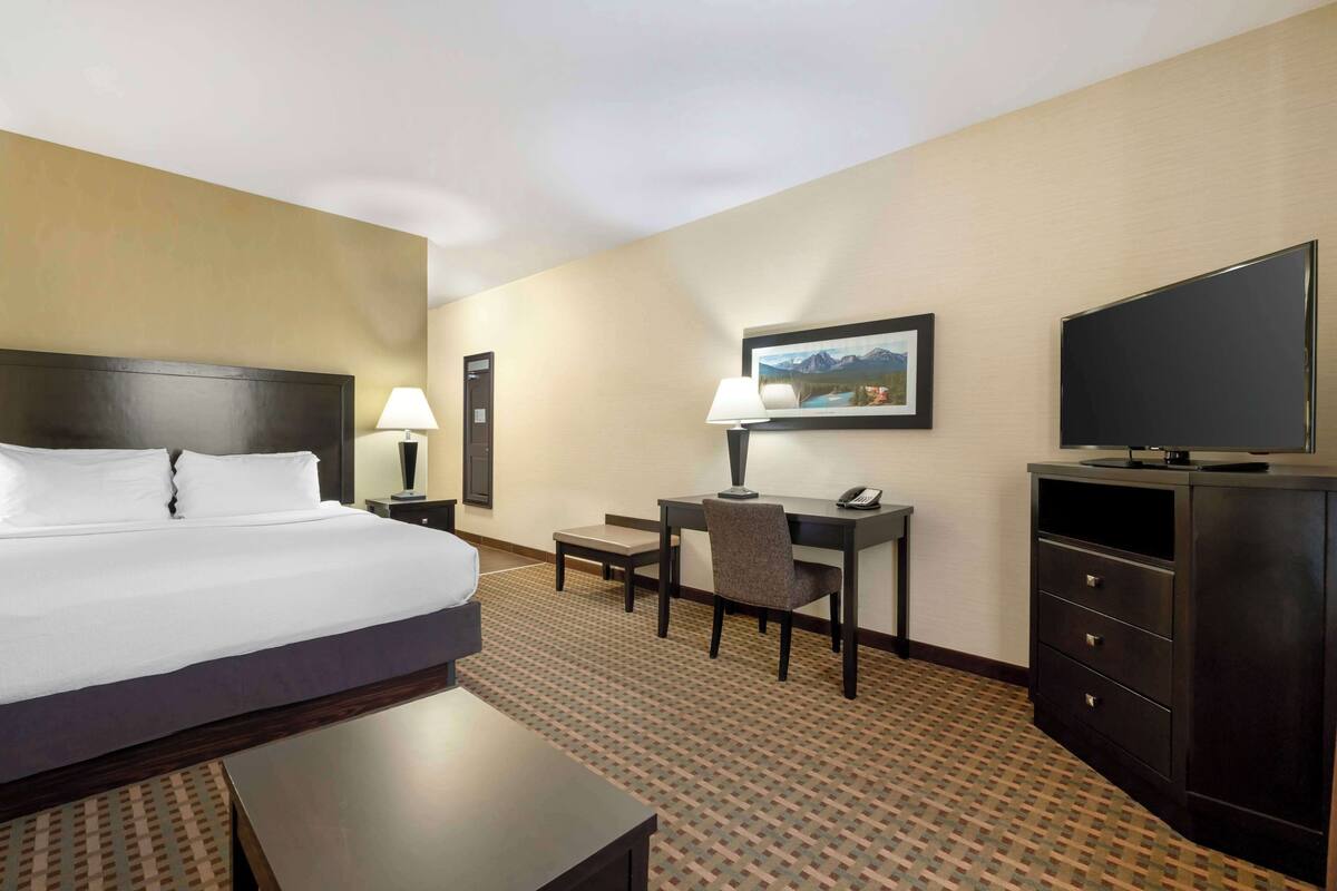 A hotel room with a large bed, a desk with a chair, a TV, and a painting on the wall.