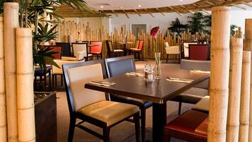Un restaurante con decoración de bambú, que incluye una gran mesa de comedor con sillas, rodeada de pilares de bambú.