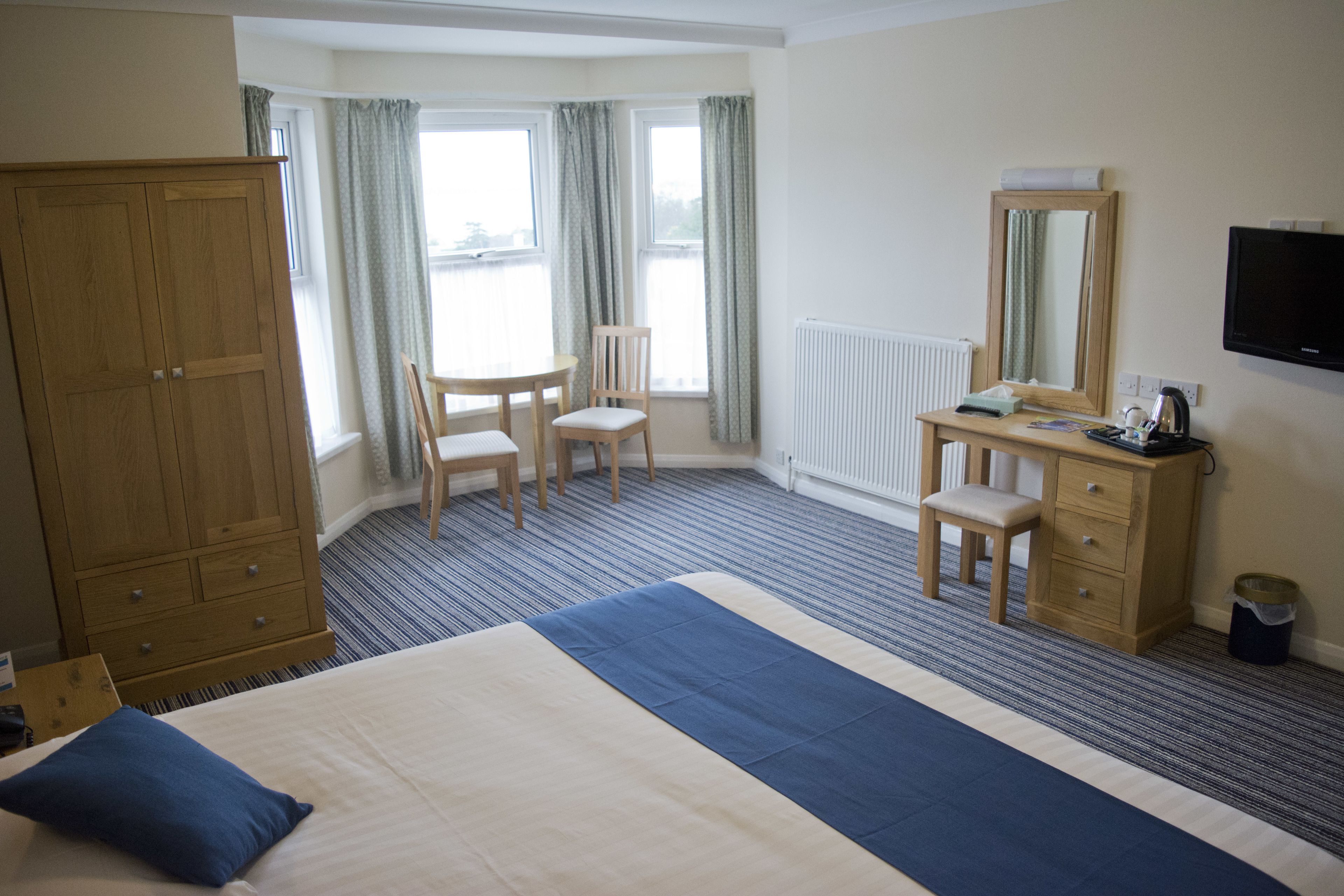 Habitación de hotel con cama, escritorio, silla, armario, espejo y televisor.