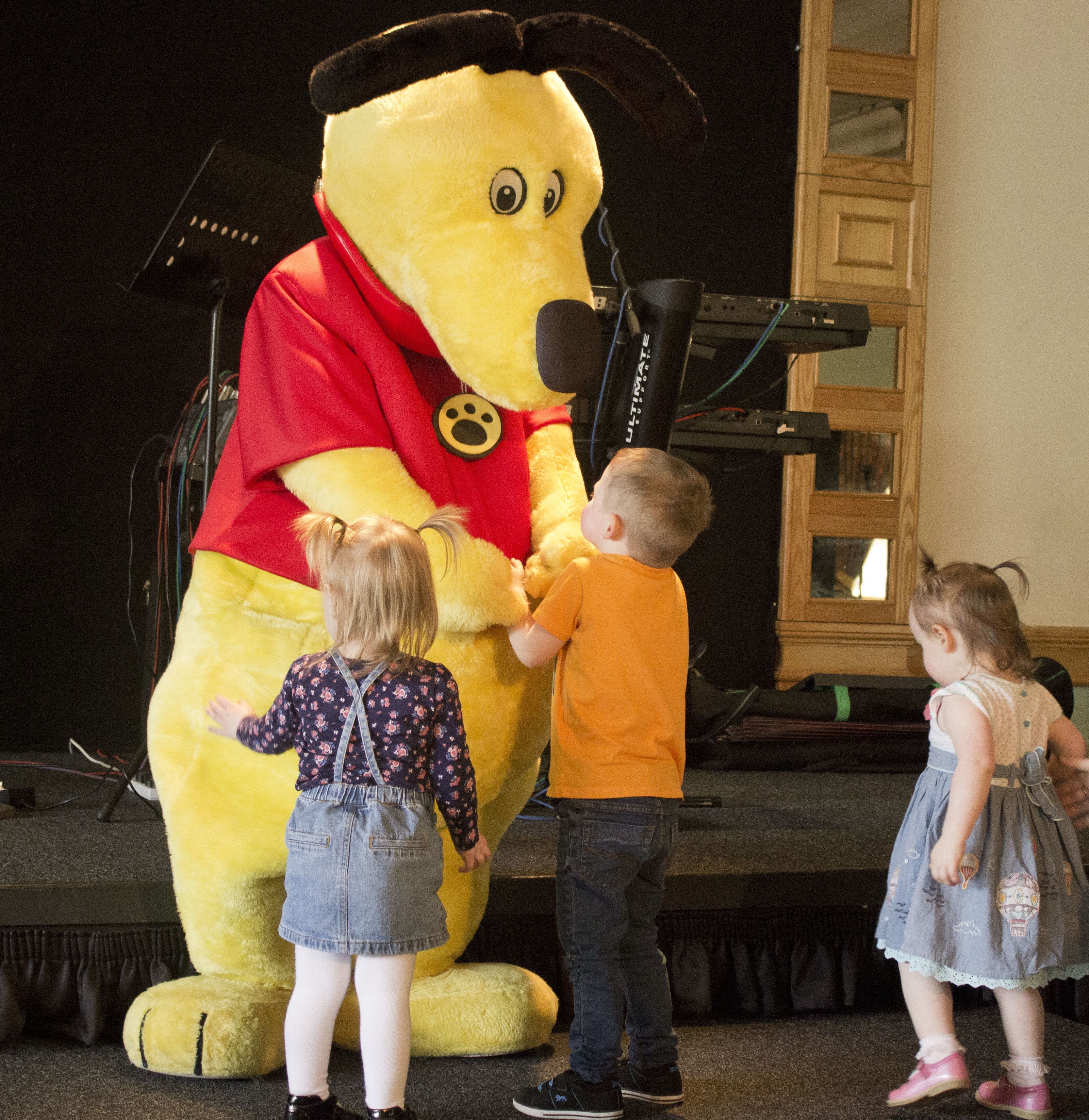 A stage with a large Winnie the Pooh mascot and two children interacting with it.