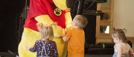A stage with a large Winnie the Pooh mascot and two children interacting with it.