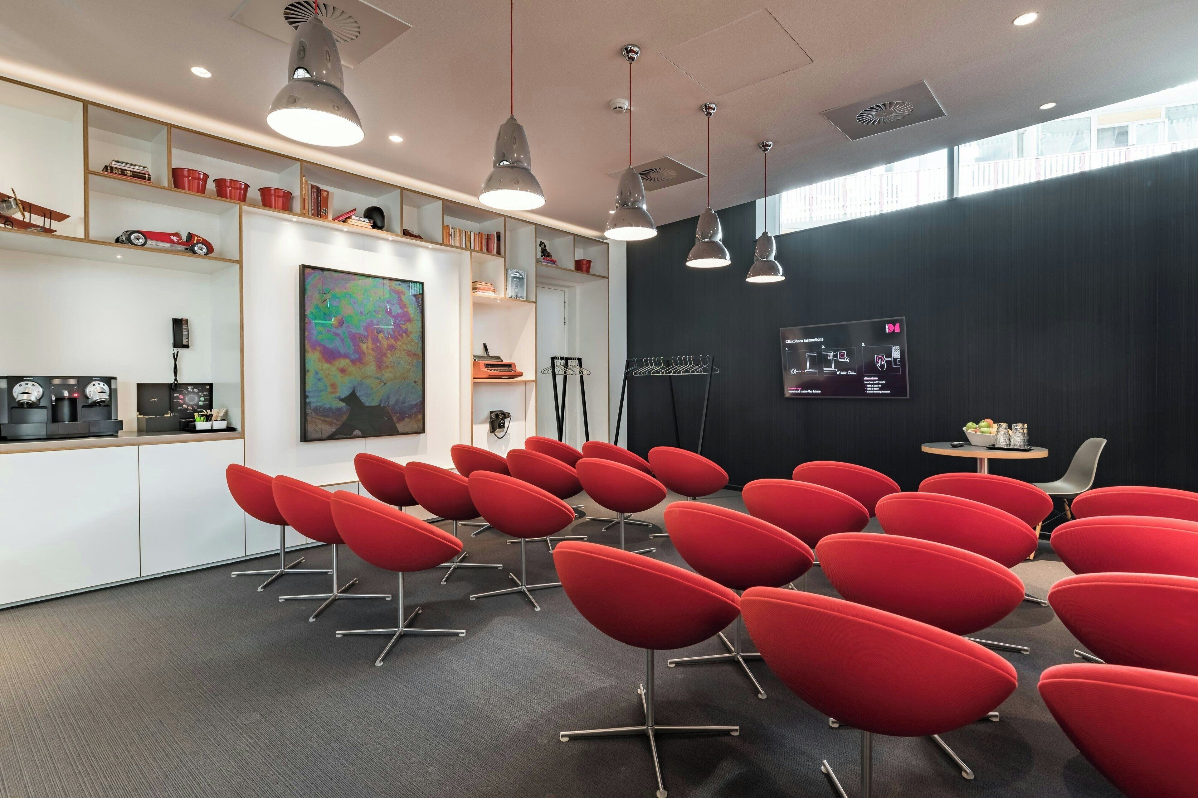 A conference room with red chairs, a large abstract painting, and a black wall with a mounted screen.