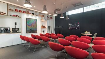 A conference room with red chairs, a large abstract painting, and a black wall with a mounted screen.