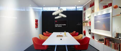 A modern conference room with a white table, red and orange chairs, and a black backdrop with the text "meet and make the future".