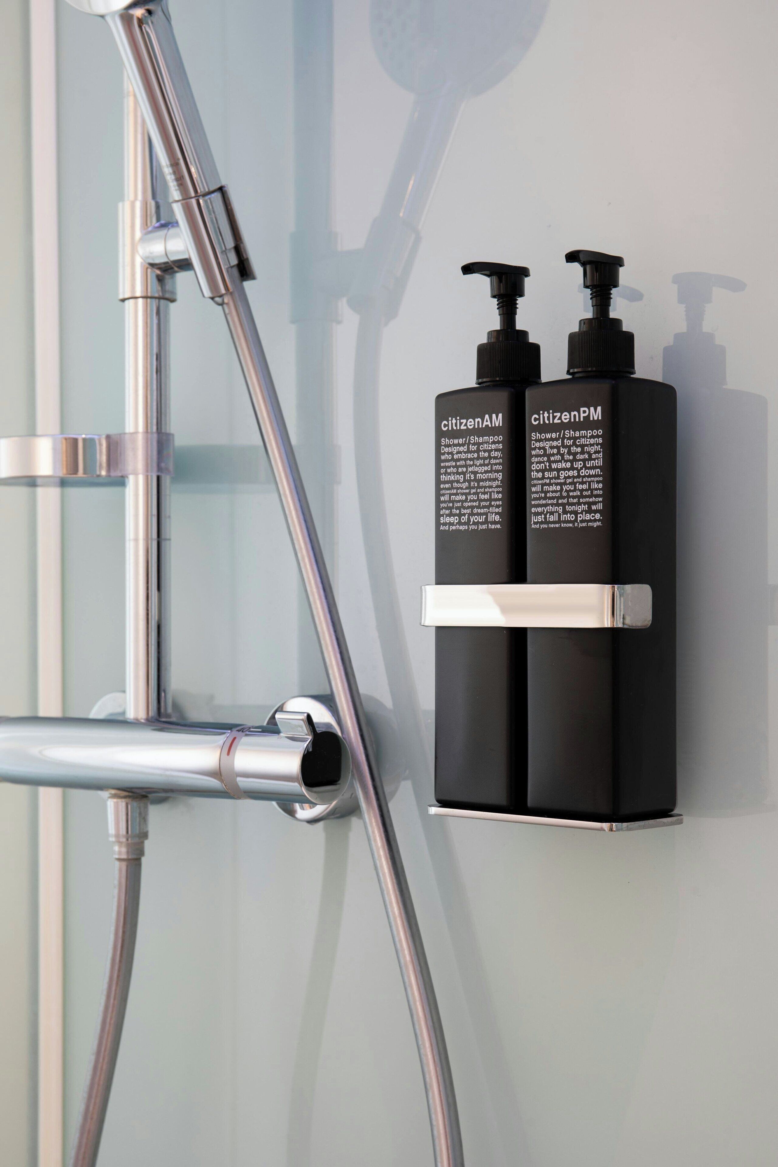 A shower with a chrome faucet and two black bottles of shower/shampoo on a wall.