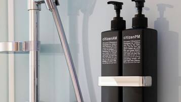 A shower with a chrome faucet and two black bottles of shower/shampoo on a wall.