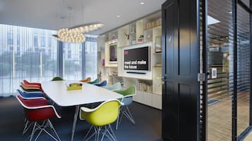 Une salle de conférence moderne, dotée d’une table blanche, de chaises colorées, d’un grand écran et d’une porte en verre donnant sur un autre espace.