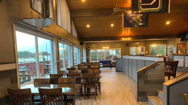 A spacious indoor area with wooden flooring, large windows offering views of the outdoors, and a bar area with a counter and stools.