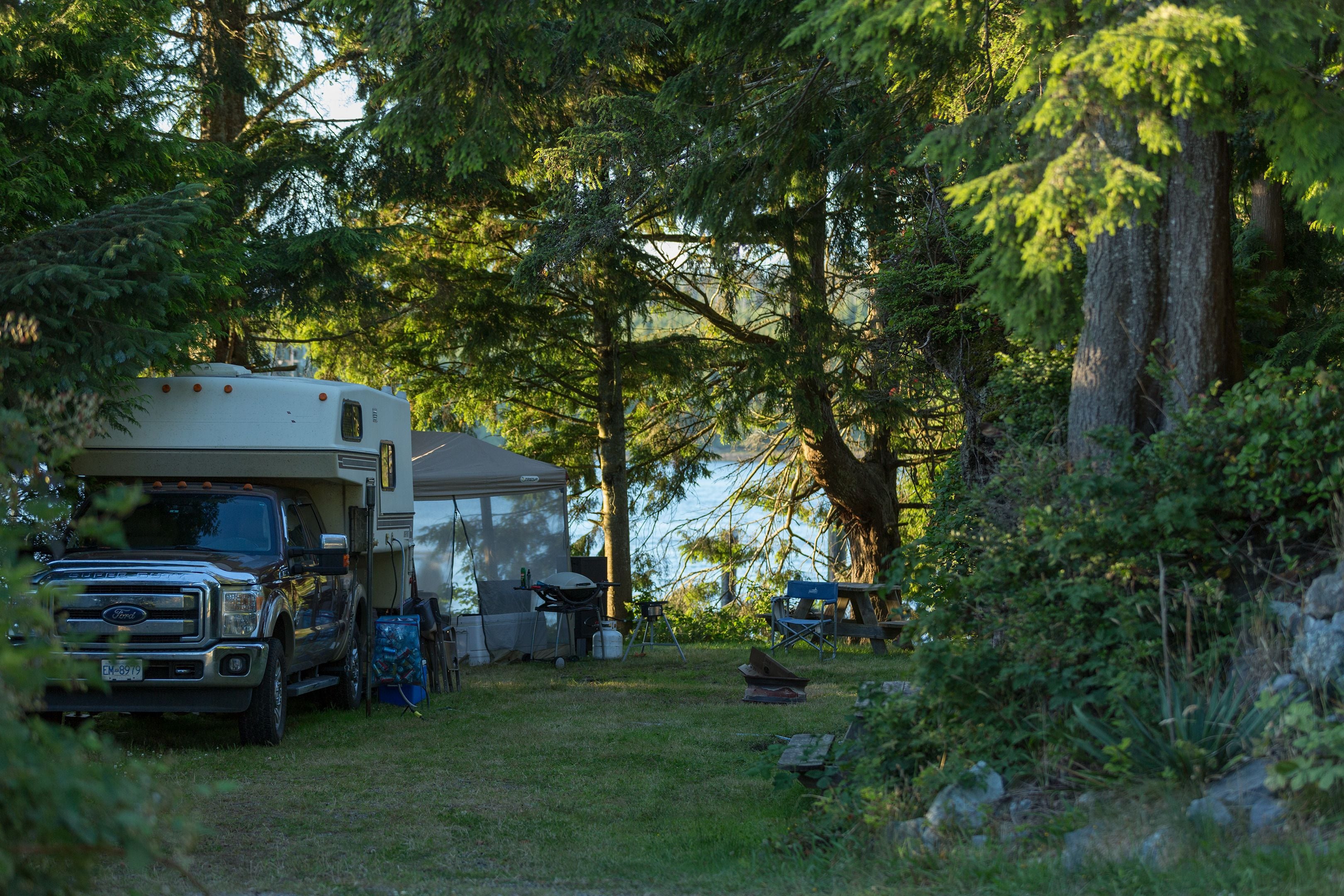 A campsite with a camper and a truck, surrounded by trees and a lake.