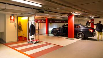 A hotel parking garage with a red pillar, a luggage cart, and a parked car.