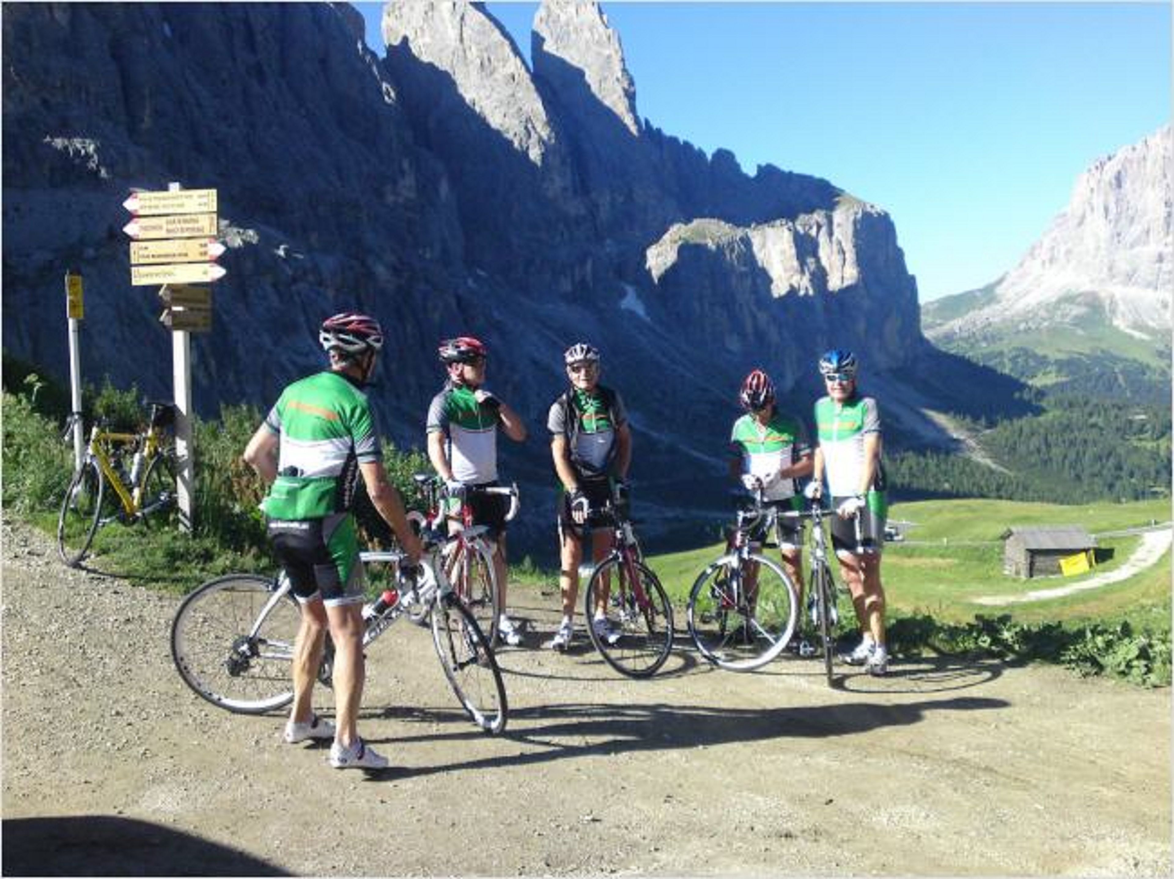 A group of cyclists on a mountain road with a signpost and a mountain backdrop.