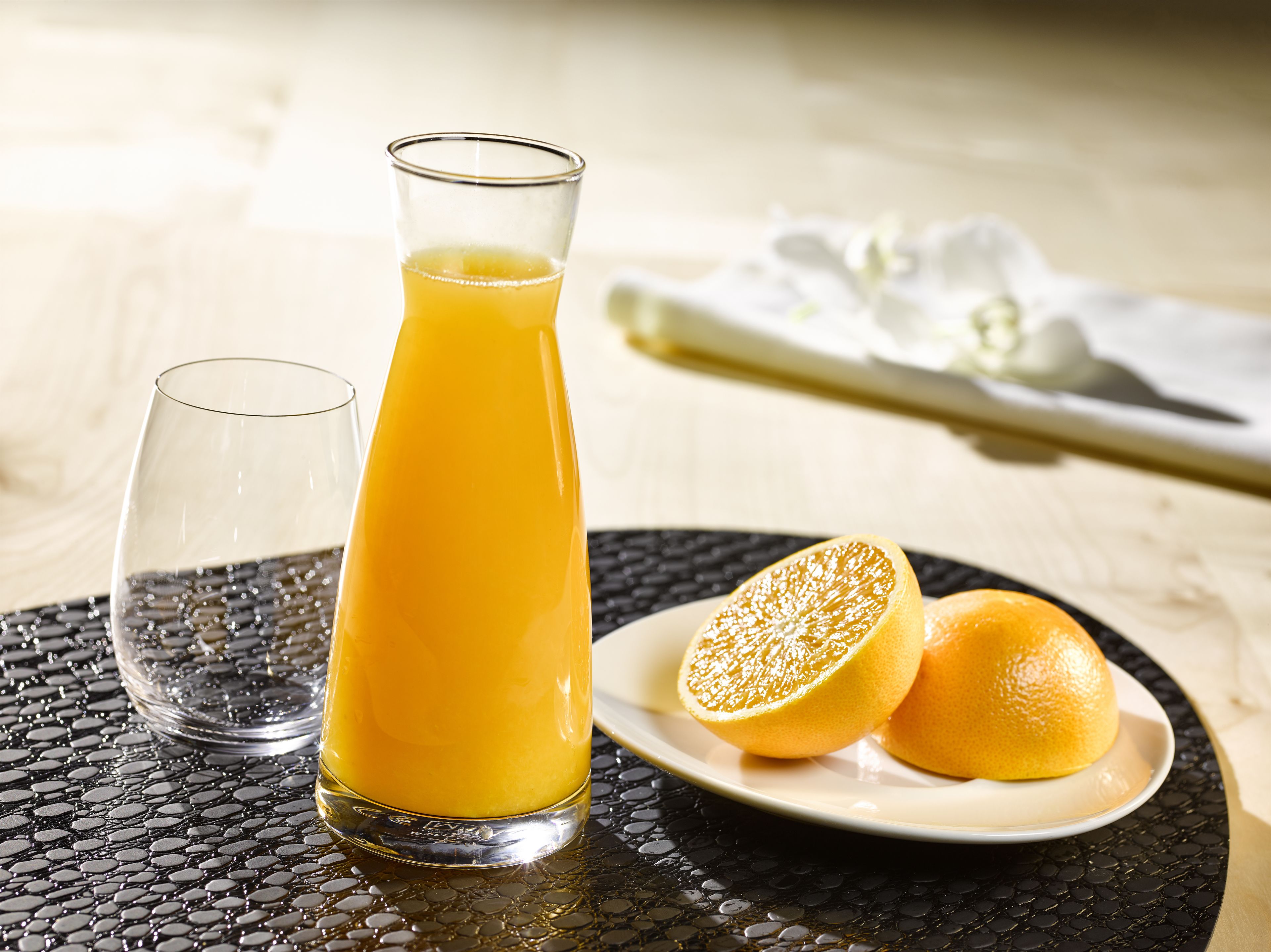 Un vaso de jugo de naranja, un vaso de agua y dos mitades de naranja sobre una mesa.