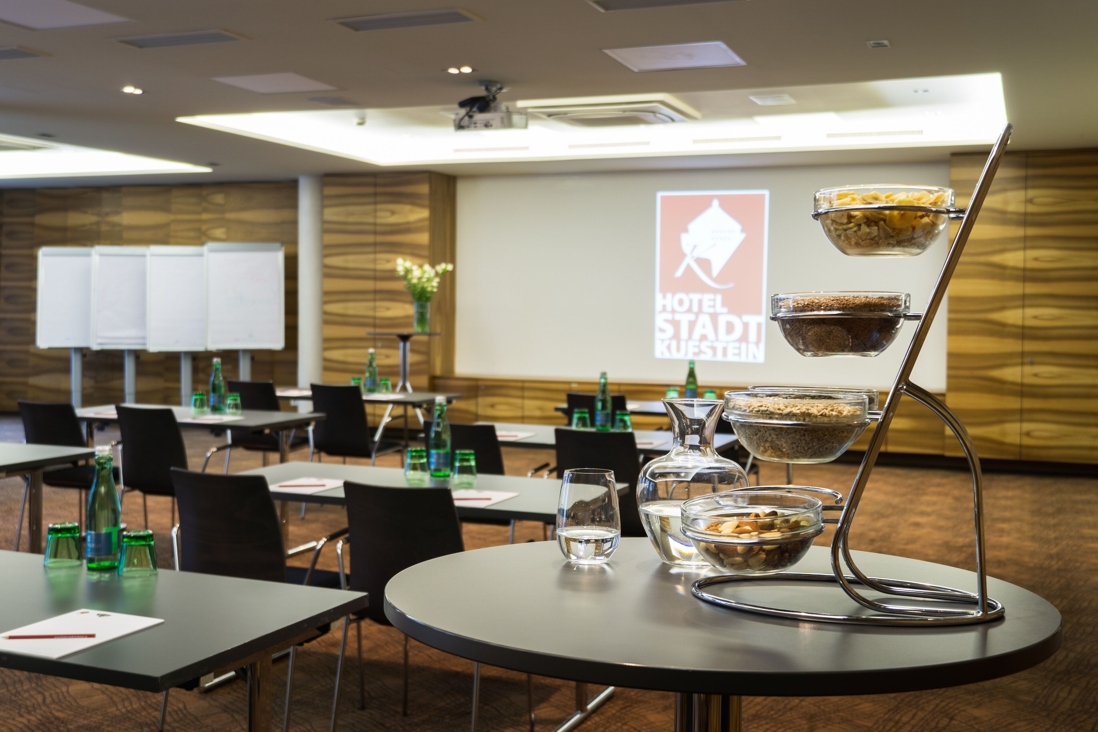 A hotel conference room with tables, chairs, and a buffet stand with bowls of food.