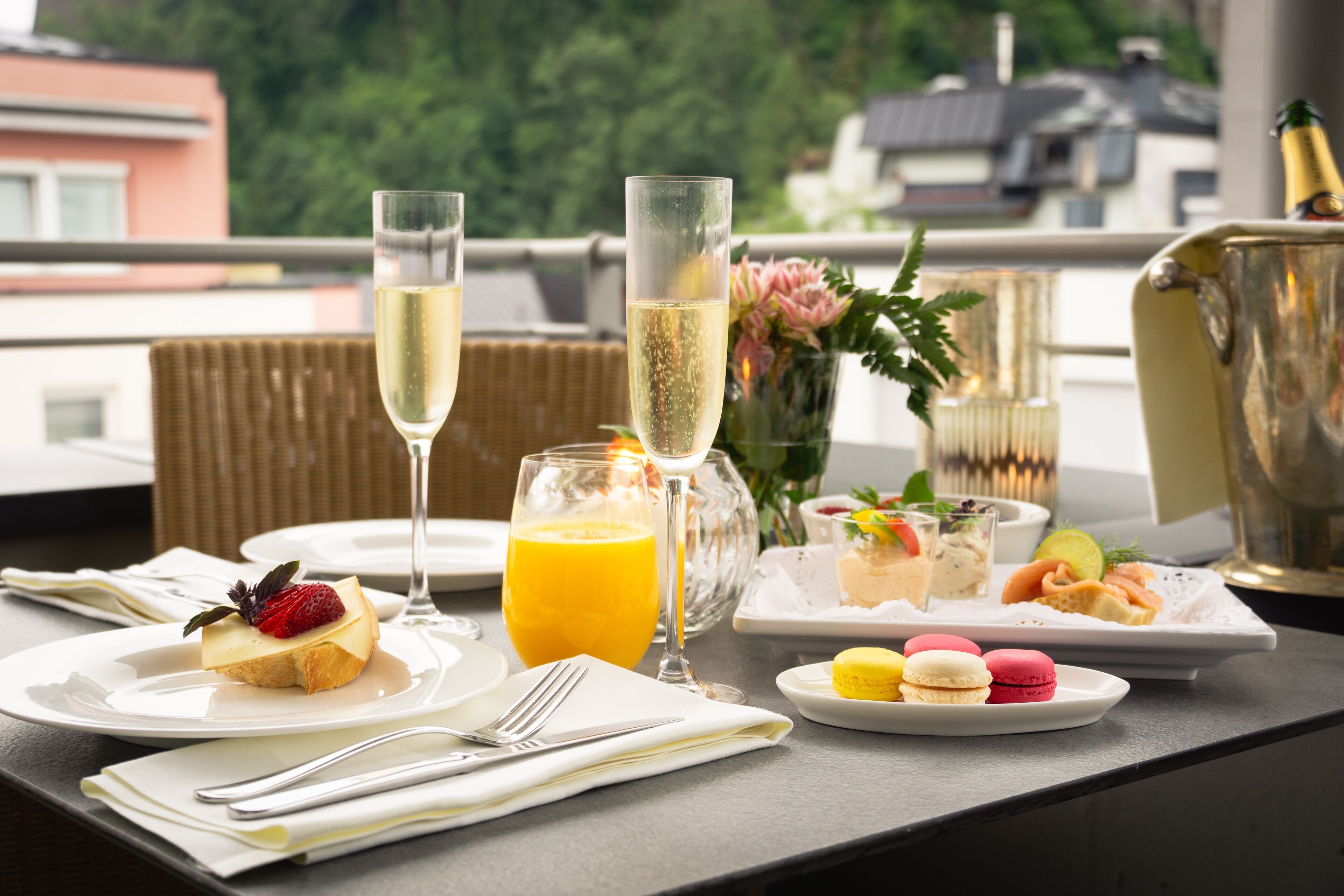 Ein Frühstücksbuffet mit Orangensaft, einem Dessert mit Erdbeere, Champagnergläsern und Macarons auf einem Tablett.