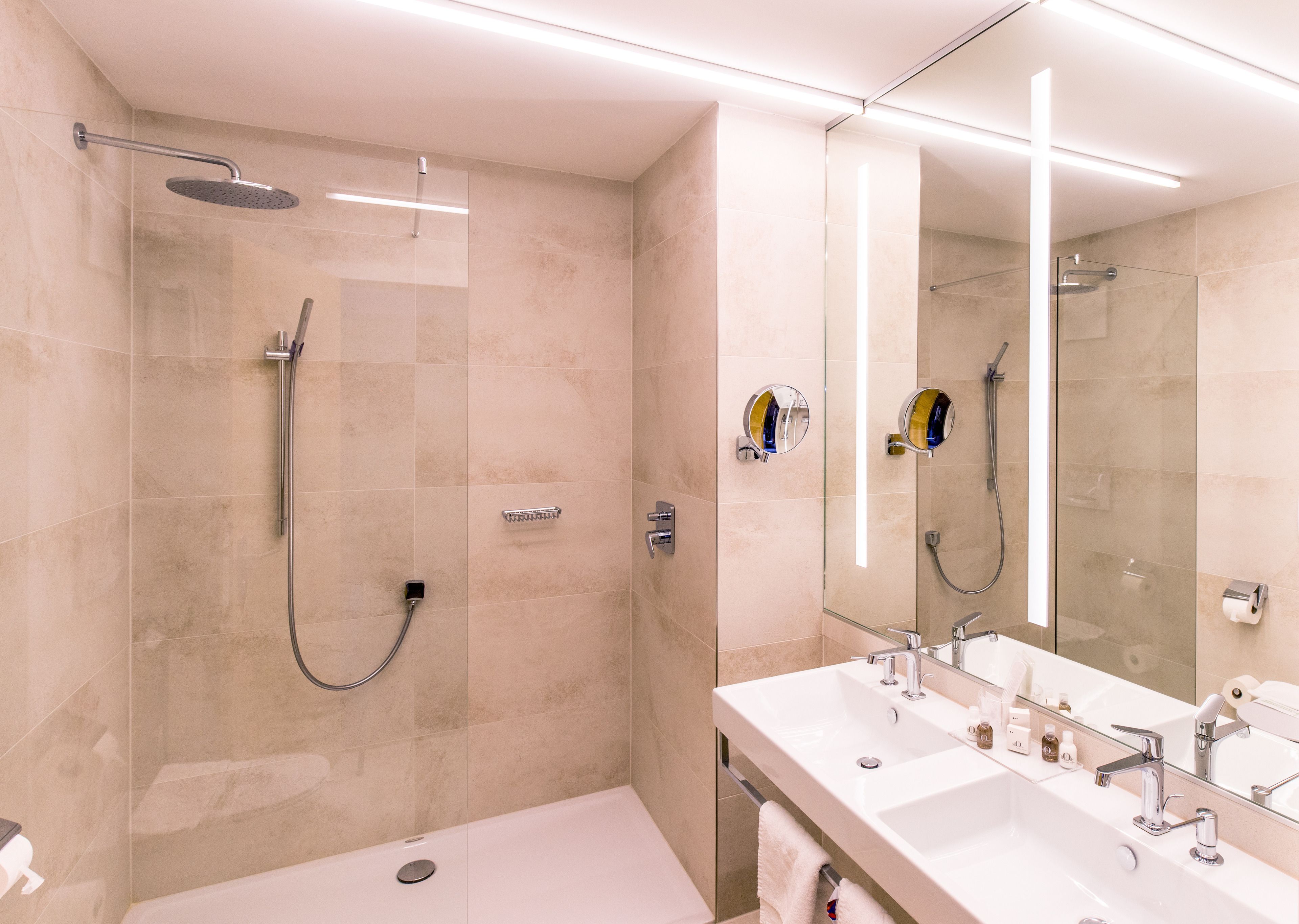 Un baño moderno con cabina de ducha de vidrio, un espejo grande y un tocador con dos lavabos.