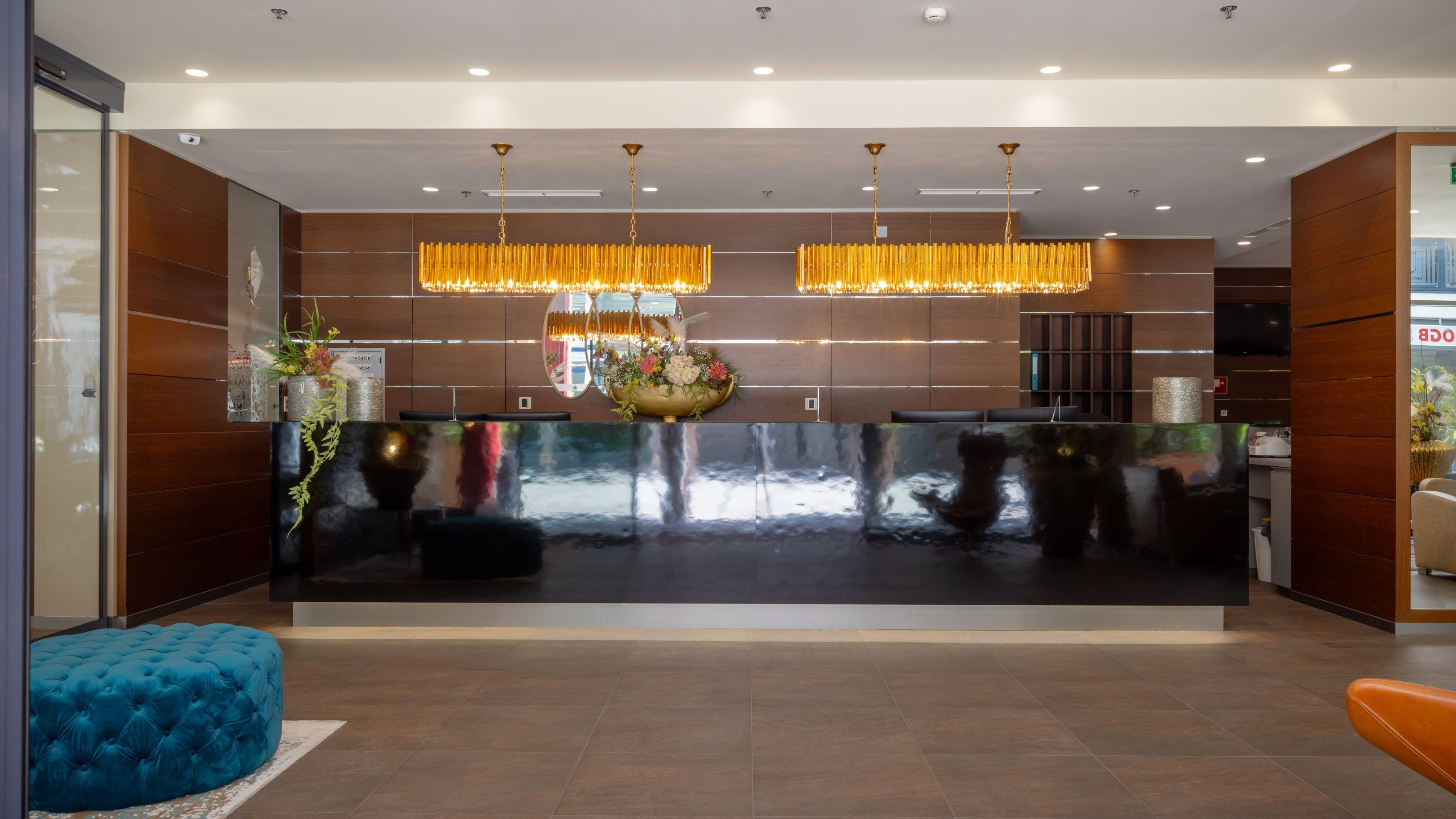 A modern reception area with a reflective black counter, wooden panel walls, and a large chandelier.