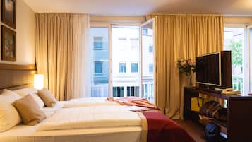 Ein Hotelzimmer mit zwei Betten, einem Fernseher, einem Schreibtisch mit Lampe und Blick auf die Stadt.