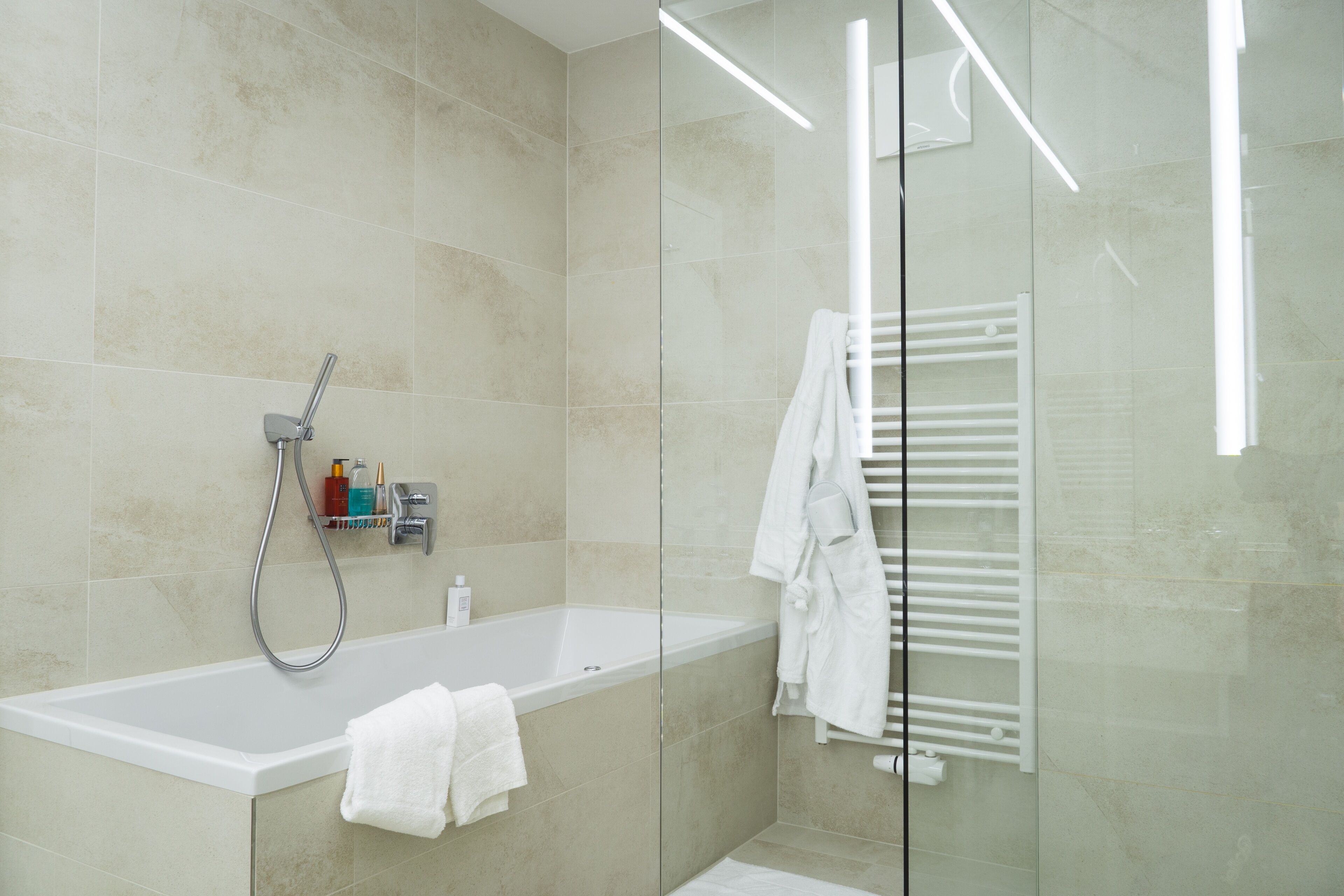Um banheiro moderno com banheira, box de vidro e porta-toalhas branco.