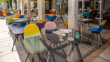 Ein Außenbereich zum Essen mit bunten Stühlen und Tischen, großen Fenstern und einem modernen architektonischen Design.